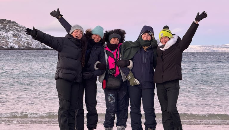 a group of people standing on a beach dressed in winter gear with fun poses and happy faces 