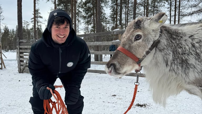 a smiling man in a black jacket next to a reindeer