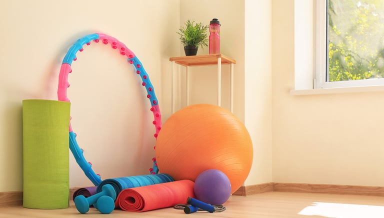 Bola, colchonete, halteres e bambolê em um espaço iluminado para exercícios.