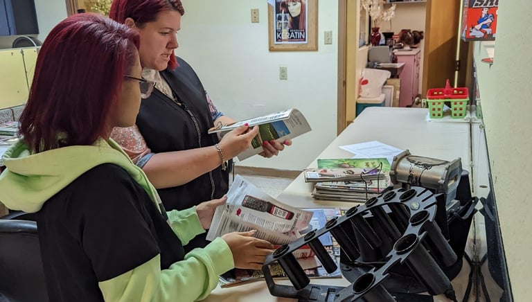 Two student hairstylists review beauty magazines and brochure inside cosmetology school..
