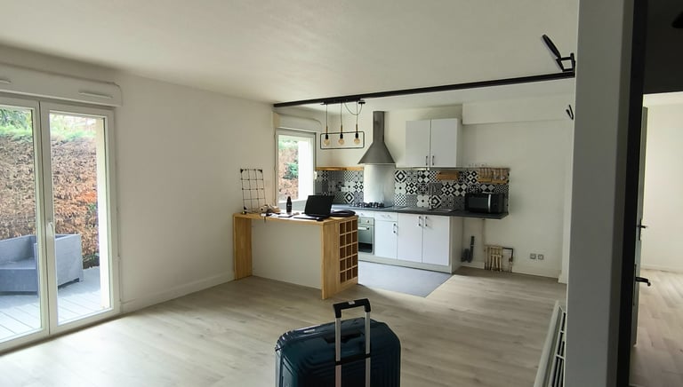 Modern open concept apartment with hardwood floors, a white kitchen, and travel luggage.