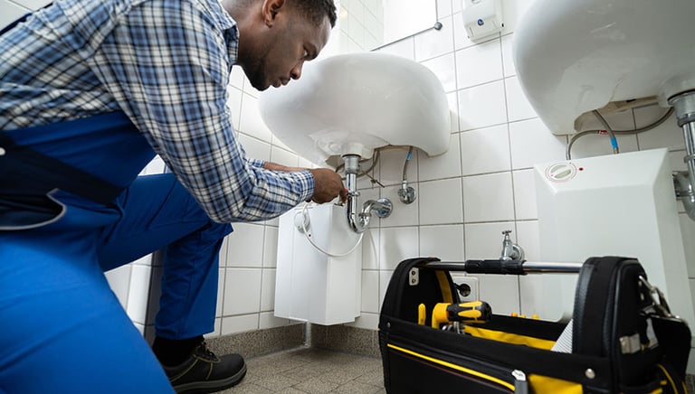 A professional plumber in London repairing a sink in a tiled bathroom, with a toolbox full of plumbi