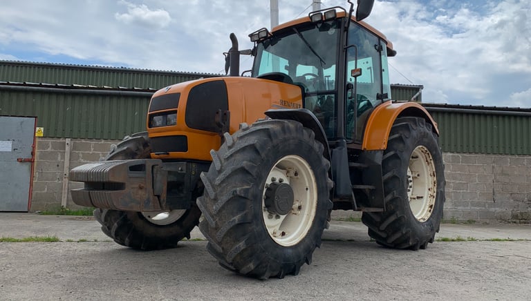 Orange Renault farm tractor parked on a concrete lot in front of an agricultural shed.