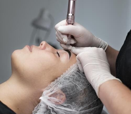 Micropigmentadora trabajando en una ceja de una mujer que esta recostada para el procedimiento