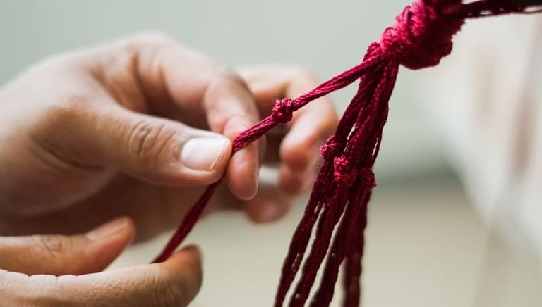 Artesana haciendo nudo decorativo con cordón rojo para un proyecto artesanal textil en macramé