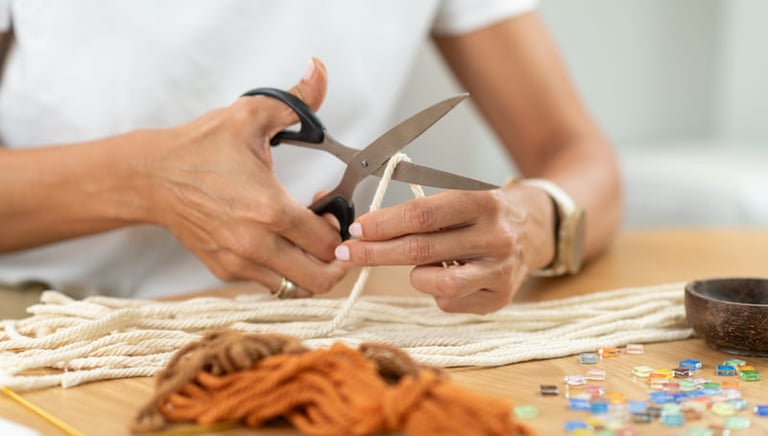 Una persona usando tijeras para cortar cordón de algodón para un proyecto artesanal de macramé.