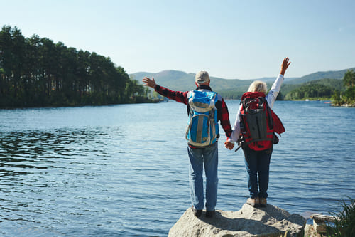 Una pareja de adultos mayores con mochilas haciendo senderismo junto a un lago de montaña