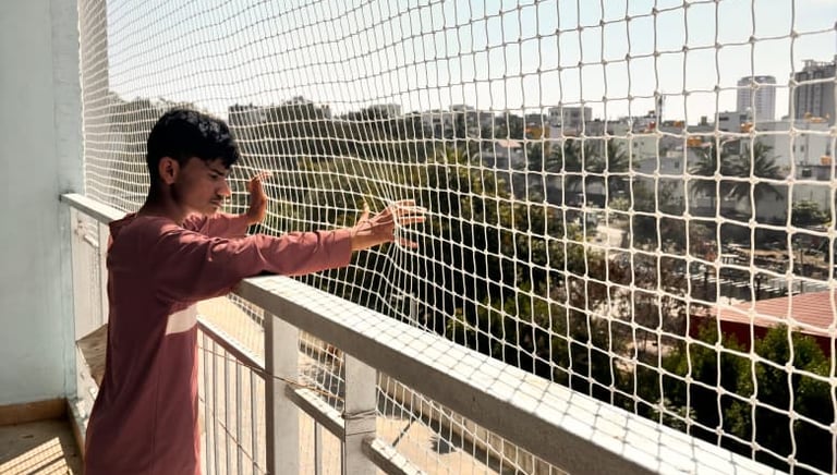 Close-up of a technician inspecting and repairing a pigeon net on a balcony.
