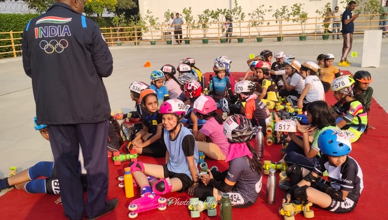 Young athletes in skating gear and helmets sit on a red mat for a speed skating workshop in India.