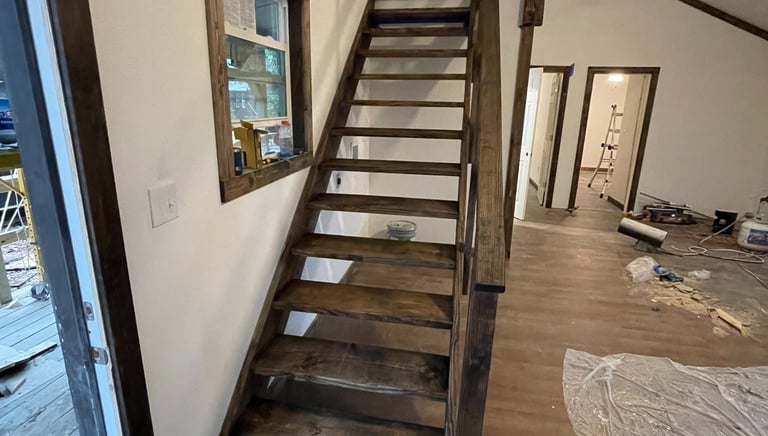 Custom dark wood staircase leading to a loft in a modern tiny house interior during construction.
