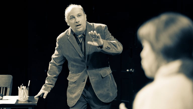 Man with hand raised walking toward woman seated in the foreground.
