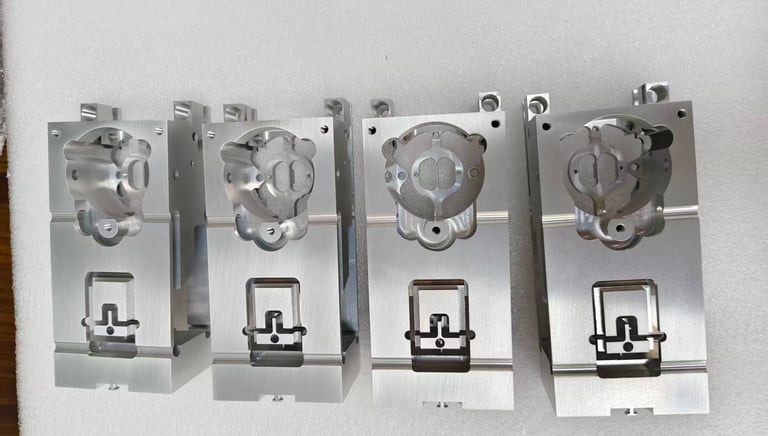 Four precision CNC machined aluminum industrial parts displayed on a white foam surface.