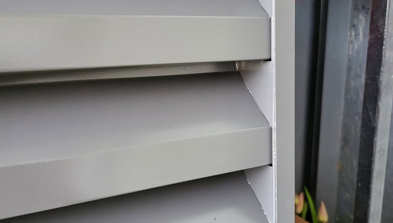 Close-up of grey exterior window shutters with fixed horizontal louvers for sun protection and ventilation.