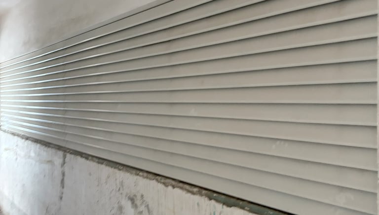 Close-up of a white metal rolling shutter door installed on a weathered concrete wall in an industrial setting.