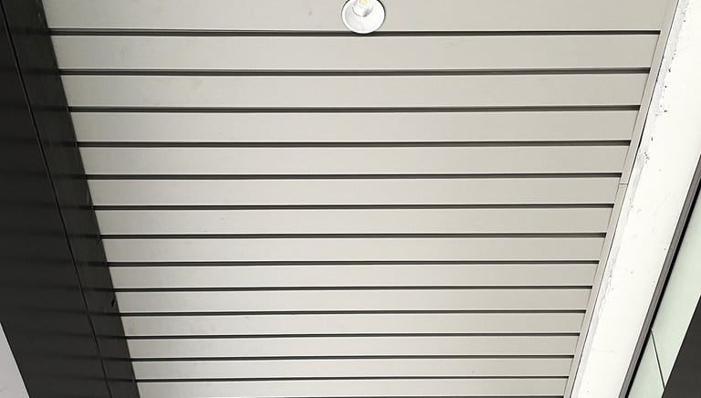 Low angle view of a modern slatted metal ceiling with an integrated LED recessed light fixture.