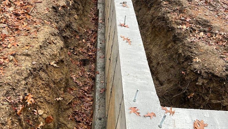 Poured concrete foundation wall with steel anchor bolts on a residential construction site.