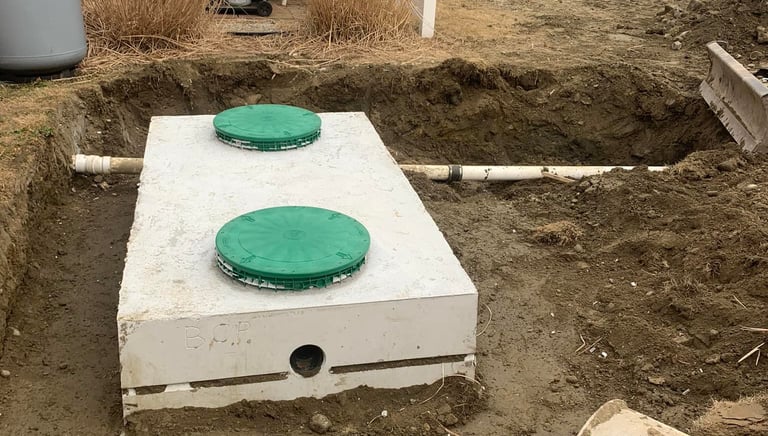 Concrete septic tank with green lids being installed in a residential backyard excavation.