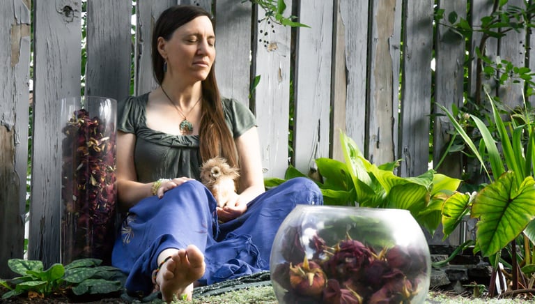 a woman sitting next to a pond surround by plants and roses holding a stuffed owl