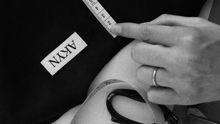 Designer Amy Powney adjusting garments on rail inside London studio