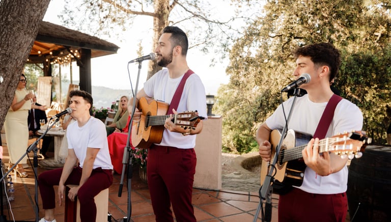 Live acoustic band with guitarists and a cajon player performing at an outdoor garden wedding reception.