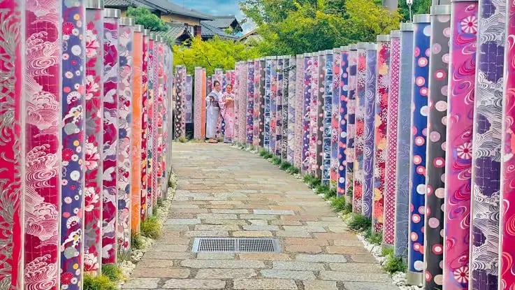 Two women in kimono walking between colorful patterned pillars in Kyoto