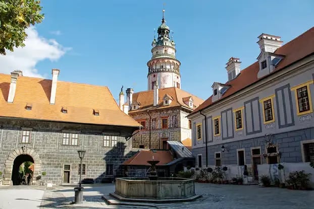 Iconic round tower of Český Krumlov Castle with fountain in sunny courtyard