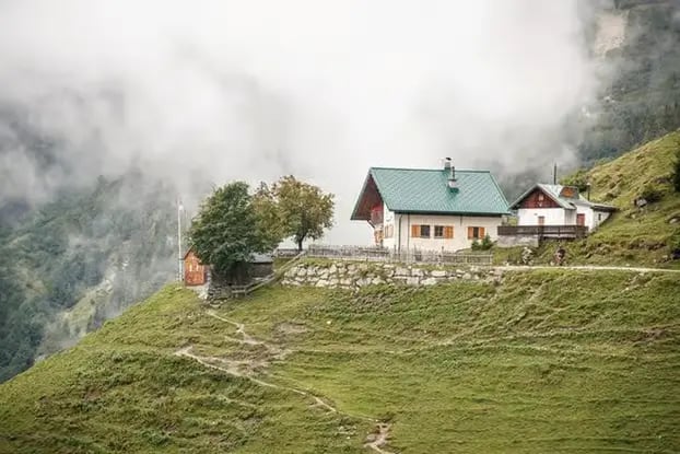 A beautiful white alpine mountain house with a green roof nestled on a grassy slope of the Nordkette mountains 