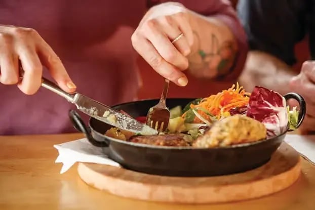 A close-up of a traveler enjoying a traditional Austrian mountain dish in a pan,