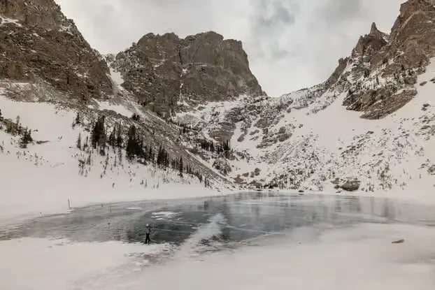 Wide view of a frozen alpine lake surrounded by dramatic snowy mountain cliffs.