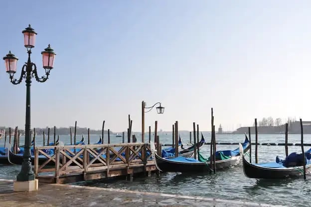 Traditional Venetian gondolas docked at a pier under a clear sky near Saint Mark's Basin.