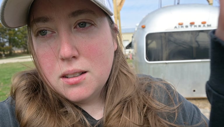 a woman in a hat standing in front of Airstream shell that is sitting on the ground