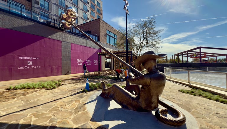 Bronze cowboy statue holding a long lasso rope in a modern outdoor urban courtyard with stone paving.