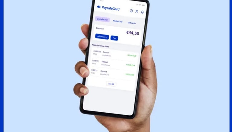 A hand holding a smartphone displaying the paysafecard app with balance and recent transactions.