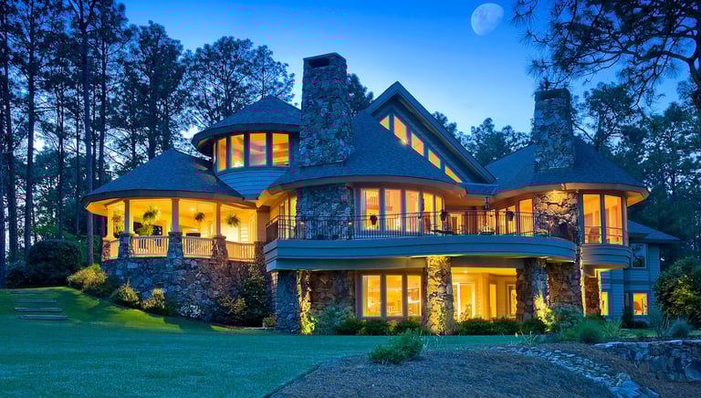 Luxury mountain estate with stone architecture and warm interior lighting under a moonlit sky.