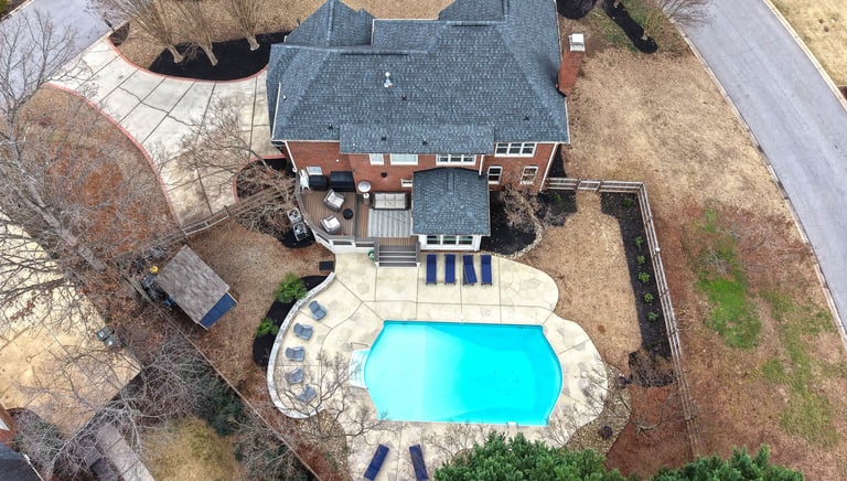 Drone Aerial view of a luxury brick home featuring a backyard swimming pool and stone patio.