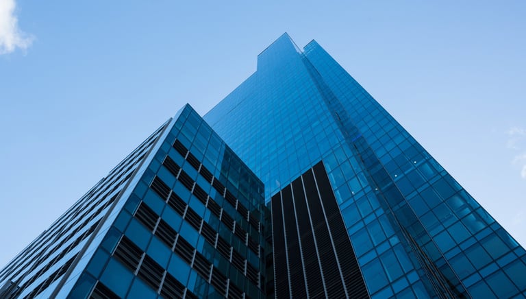Low angle view of a modern blue glass skyscraper and office building against a clear sky.