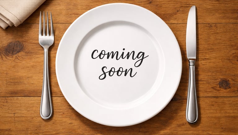 A white plate with “Coming Soon”, with a fork on the left and knife on the right.