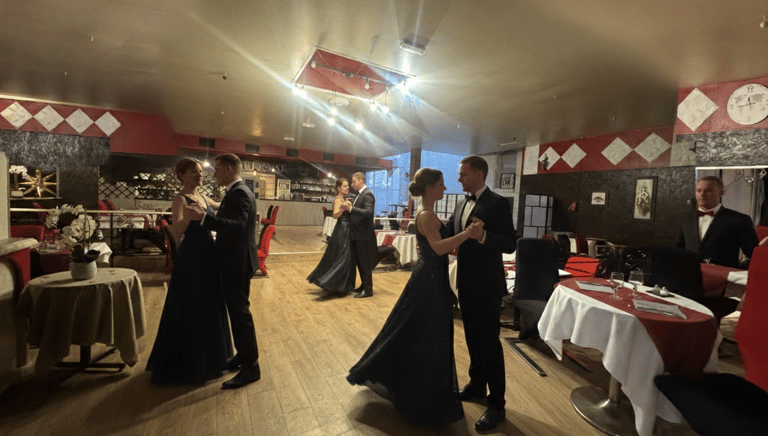 Couples in formal black-tie attire dancing in a ballroom at an elegant gala dinner event.