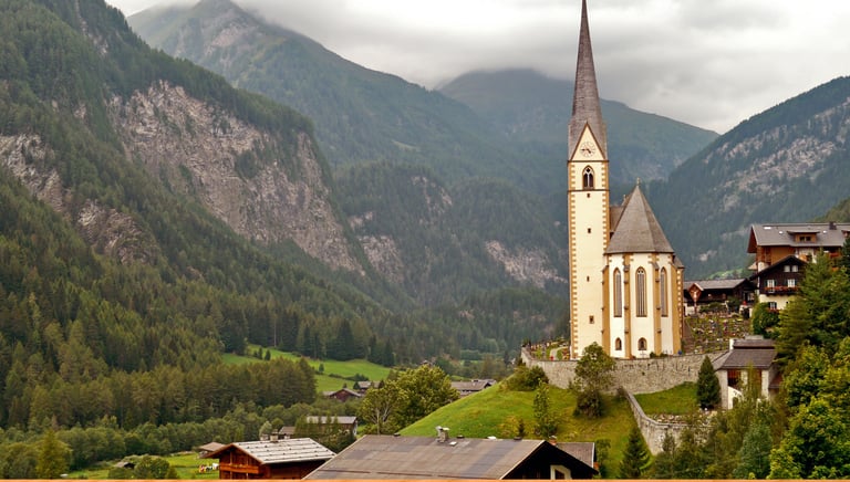 A scenic view of St. Vincent Church in the Austrian Alps village of Heiligenblut during a cloudy day.