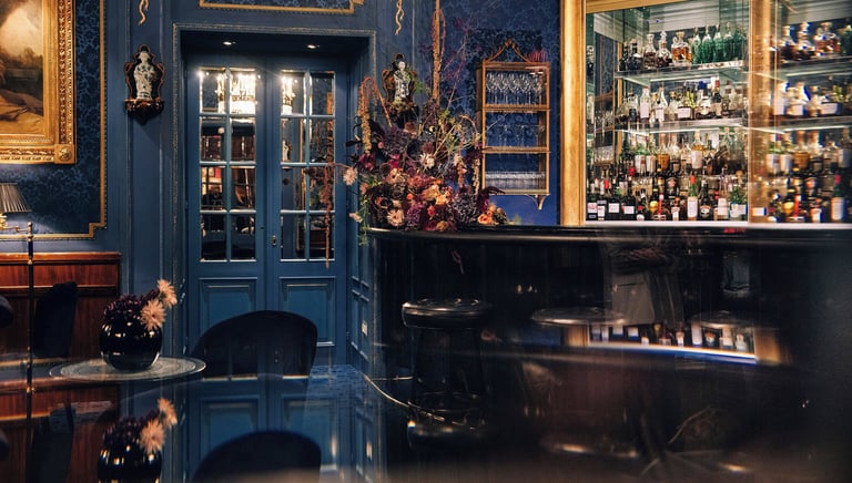 Elegant luxury bar interior featuring blue damask wallpaper, a gold liquor cabinet, and a crystal chandelier.