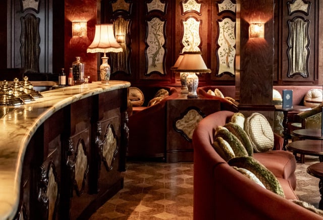 Elegant vintage hotel bar with marble counter, plush seating, and warm ambient lighting.