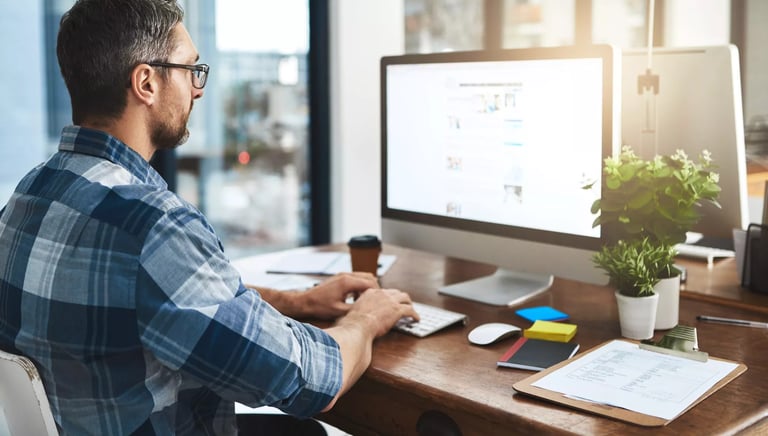 a man sitting at a desk with a computer and a coffee cup