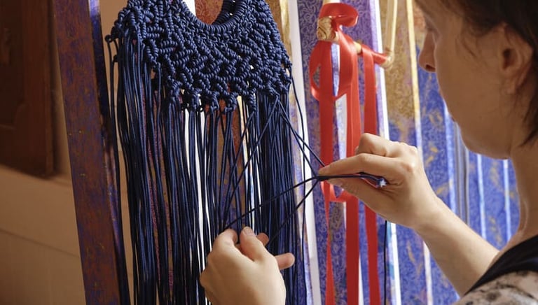 Handmade navy blue macrame bag being woven by an artist using intricate knotting techniques.
