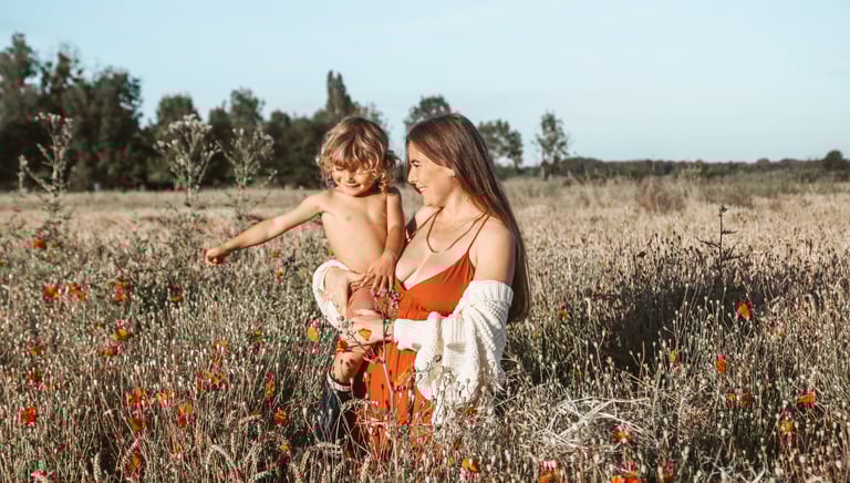 photo d'une maman en robe rouge portant son enfant torse nu dans un champ de coquelicots