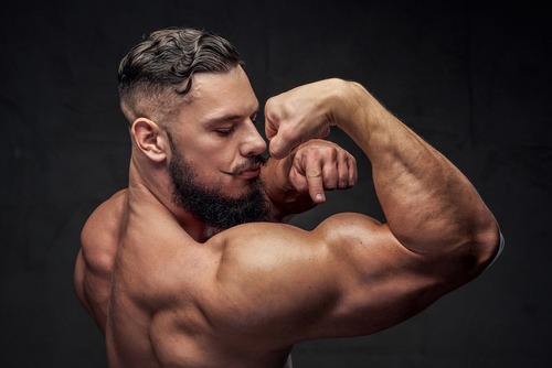 A muscular man with a groomed beard and mustache flexing his large bicep and back muscles.