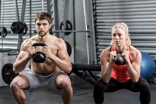 A fit man and woman performing kettlebell goblet squats during a strength training workout at the gym.
