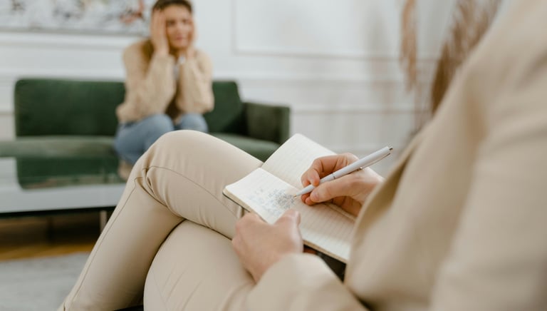Distressed woman sitting on a couch in an office with a therapist who is taking notes