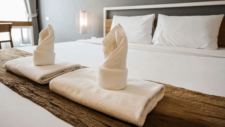 Quarto de hotel com cama branca cuidadosamente feita, mostrando um ambiente limpo e acolhedor