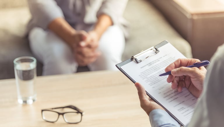 Zwei Personen in einer Psychotherapiesitzun. Der Psychotherapeut macht sich Notizen.
