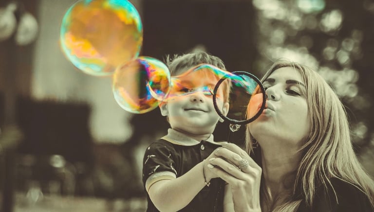 Nanny and child blowing bubbles in a park